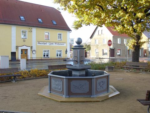 Das Bild zeigt in der Bildmitte einen alten Brunnen auf dem Dorfplatz des Ortes Löbnitz.