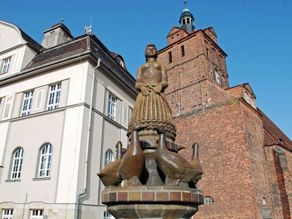 Dommitzsch - Gänsebrunnen, zu sehen ist der Brunnen mit der Statue einer Gänsemagd umringt von Gänsen, im Hintergrund sieht man den Ratskeller und die St. Marien Kirche © LTM, Jasmin Rhein