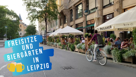 Ein Fahrradfahrer fährt an mehreren Gastronomien mit Freisitzen vorbei, in denen zahlreiche Gäste sitzen.