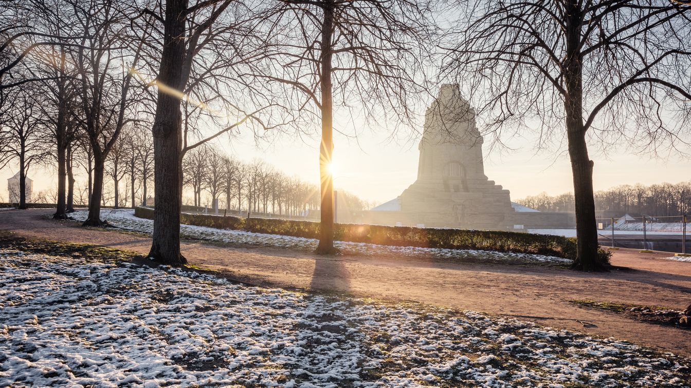 Blick auf die winterliche Umgebung mit dem monumentalen Völkerschlachtdenkmal bei Sonnenaufgang im Hintergrund.