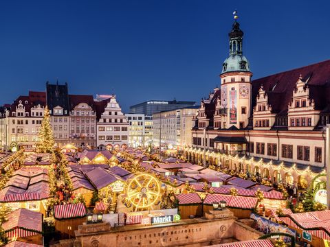 Das Alte Rathhaus Leipzig ist im Hintergund zu sehen. Davor gibt es viele weihnachtlich geschmückte Buden, die verschiedene Handwerkskunst und Süßigkeiten anbieten. Es ist Abend.
