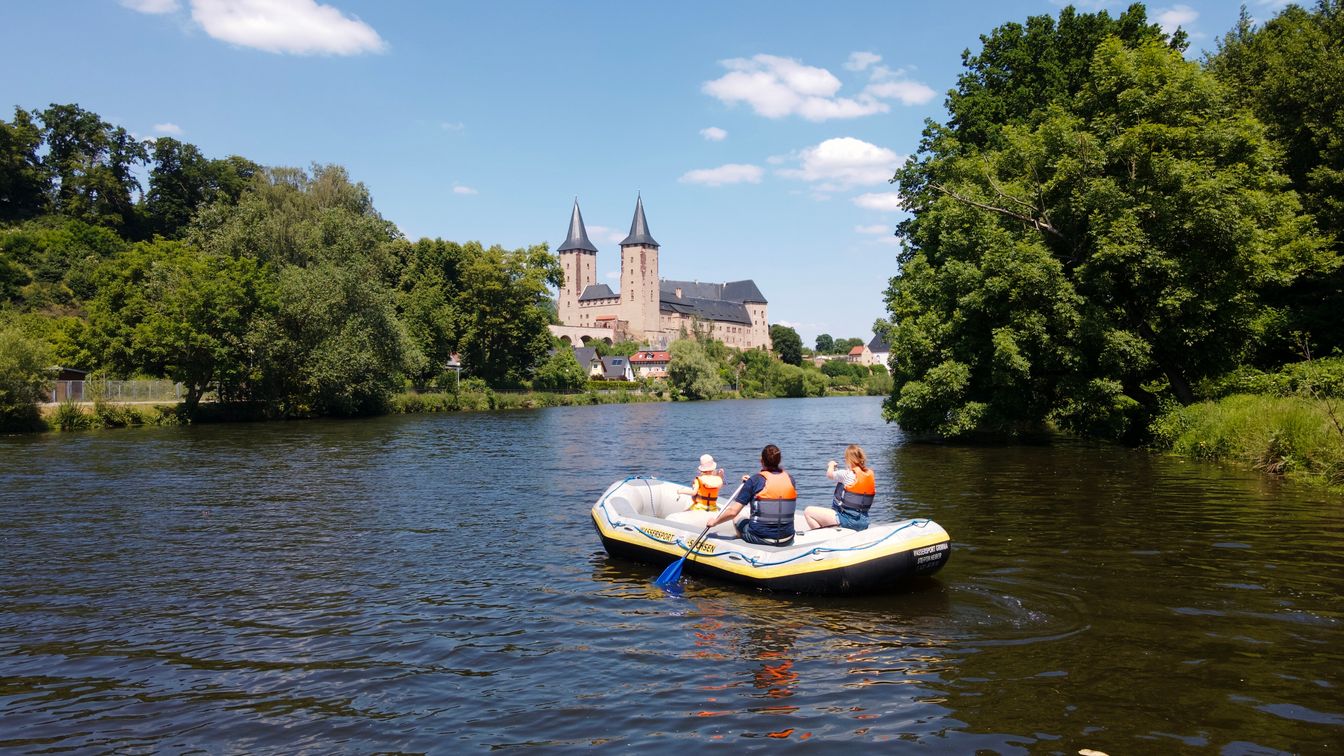 Eine Familie sitzt in einem Schlauchboot und paddelt auf der Mulde dem Schloss Rochlitz entgegen.