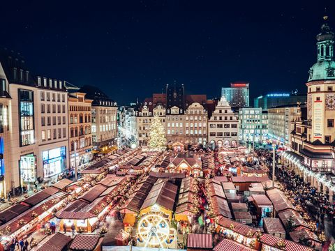A birds-eye view of the brightly lit Christmas Market in Leipzig market square by night with countless stalls and visitors.