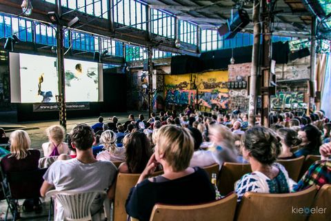 Umgeben von bemalten Wänden schauen viele Besucher einen Film, Open Air Kino in Leipzig, Sommer