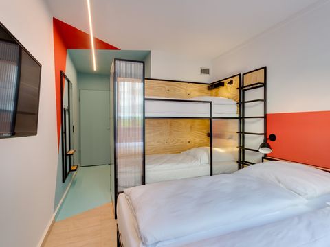 Blick auf ein modernes Hostelzimmer mit einem Doppelbett, einem Etagenbett und einem Wandfernseher.