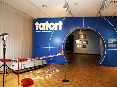 Eingang zur Ausstellung "Tatort. Mord zur besten Sendezeit" mit dem Setting eines echten Tatorts & im Design der beliebten Fernsehserie "Tatort" - Foto: Julia Franke