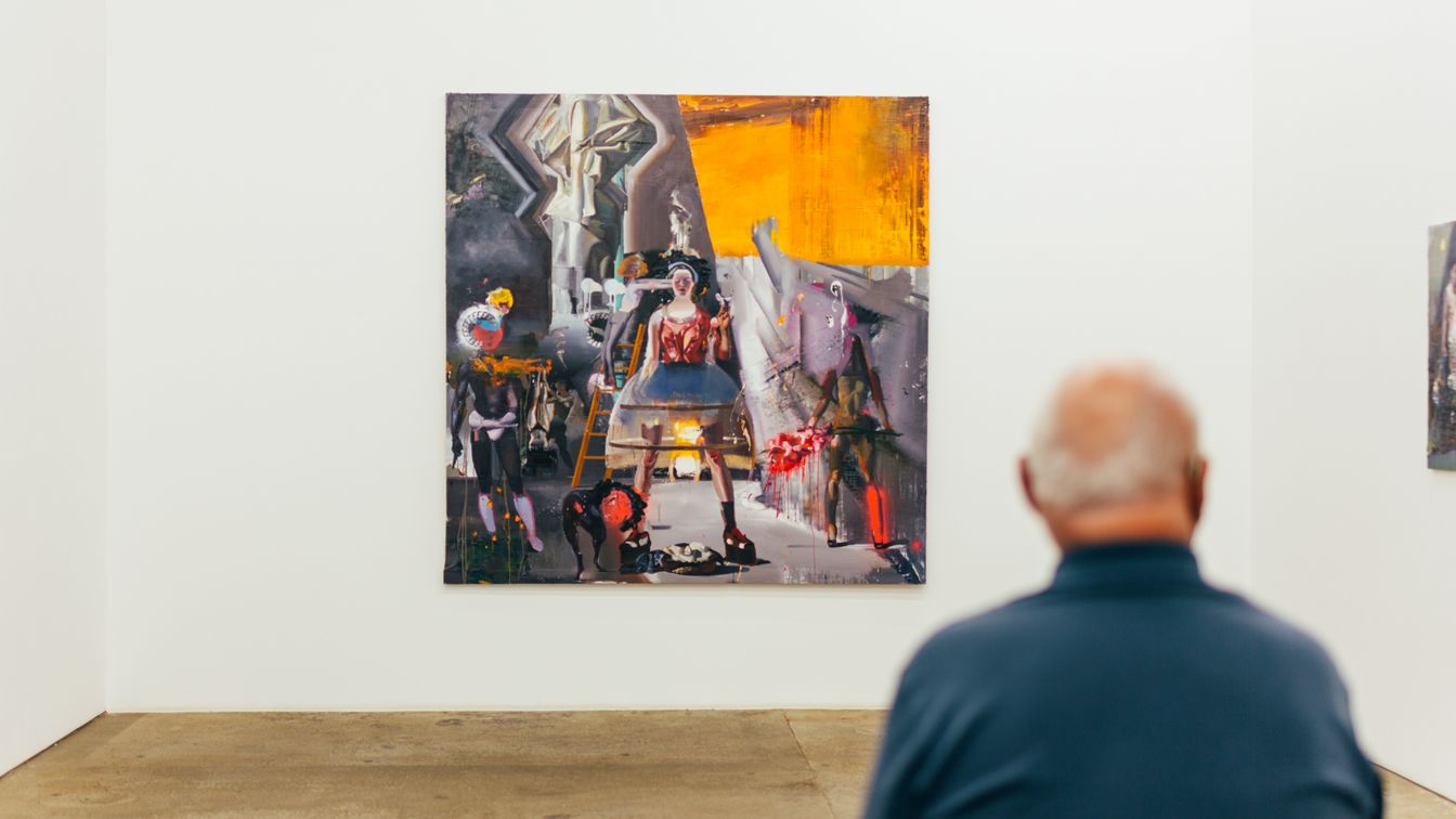 Ein älterer Mann sitzt in einer Galerie in der Spinnerei vor einem abstrakten Gemälde einer Frau