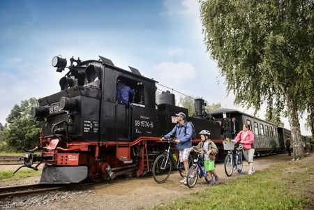 Das Bild zeigt eine junge Familie mit Fahrrädern, dahinter die schwarz-rote Lok der Döllnitzbahn.