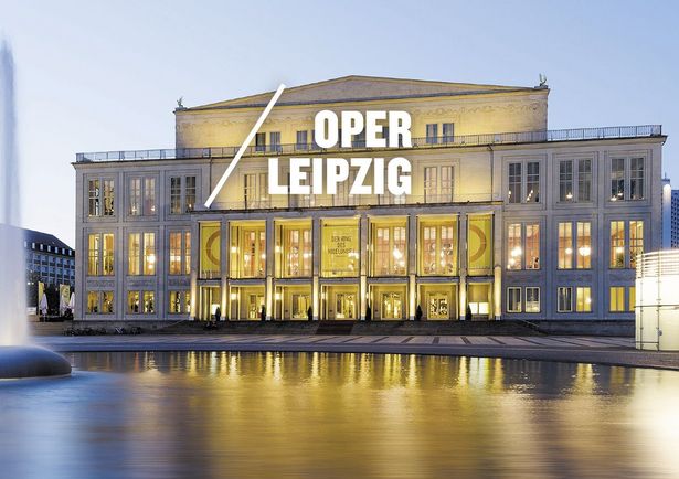 View of the illuminated Leipzig Opera behind the fountain at Augustusplatz with yellow flags at the Opera heralding the Wagner Festival in Leipzig, City of Music.