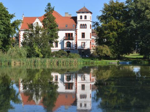 Die weiß-rote Renaissance Fassade des Schloss Thammenhain spiegelt sich im Schwanenteich des Schlossparks.
