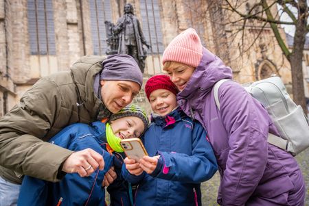 Eine Familie informiert sich über das Bach-Denkmal vor der Thomaskirche mithilfe der Explore Leipzig App.
