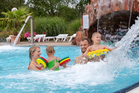 Eine lachende Familie mit Kindern hat Spaß in einem Pool des Freizeitbad Riff, in dessen Resort Familien für einen Kurzurlaub auch übernachten können.