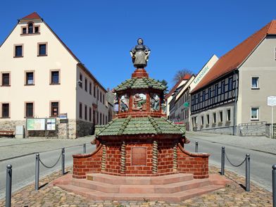 Kohren-Sahlis - Töpferbrunnen, zu sehen ist der Brunnen aus roten Ziegelsteinen, mit zwei grünen Dächern und einer Töpferin mit ihren Erzeugnissen © Andreas Schmidt