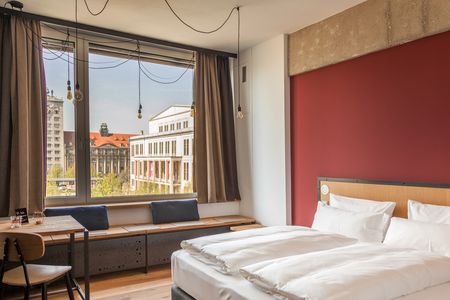 Modernes Hotelzimmer in den Felix Suiten Leipzig mit Doppelbett und großem Fenster, welches den Blick auf die Oper Leipzig ermöglicht