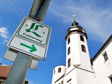 Der Lutherweg Sachsen, zu sehen ist die Wegmarkierung (Schild) des Lutherwegs, daneben die Stadtkirche St. Marien in Torgau © Andreas Schmidt