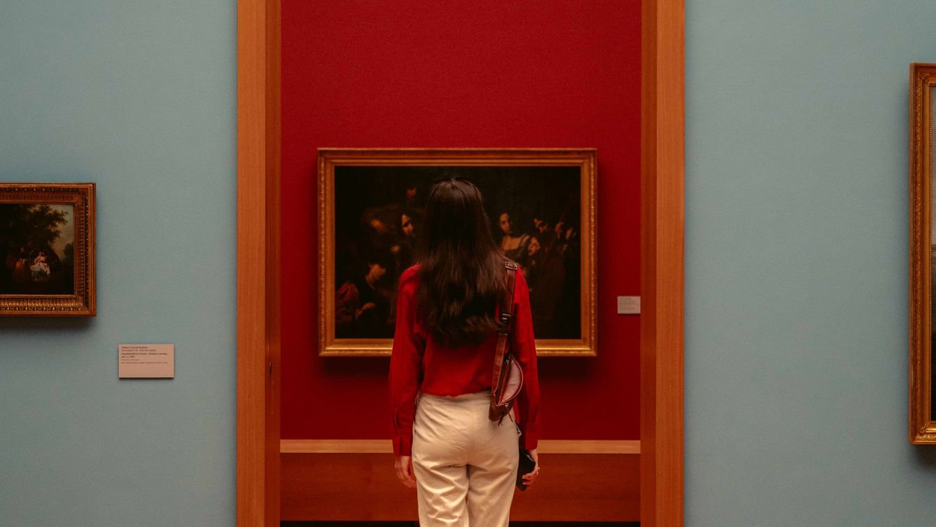 Eine Person geht durch einen sehr hohen Türrahmen und betritt einen neuen Ausstellungsraum, sie steht direkt vor einem Gemälde