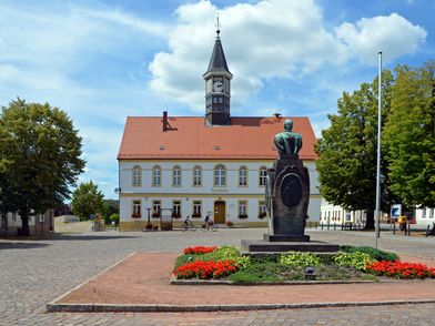 Schildau - Rathaus und Gneisenaudenkmal, zu sehen ist das Denkmal mittig auf dem Marktplatz umringt von einer Blumenbepflanzung, im Hintergrund steht das Rathaus © Andreas Schmidt