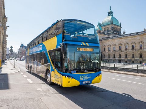 Ein blau-gelber Bus von Stadtrundfahrt Leipzig GmbH steht bei einer Bustour vor dem Bundesverwaltungsgericht