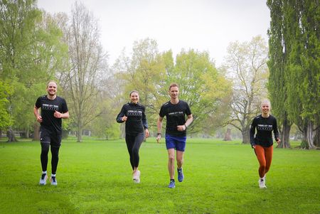 Vier Personen joggen der Kamera in einem Park entgegen
