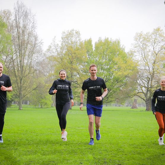 Vier Personen joggen der Kamera in einem Park entgegen
