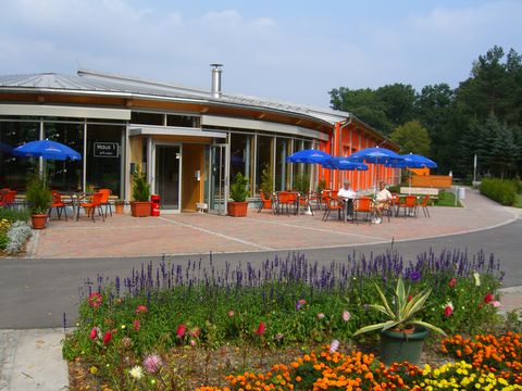Blick auf das Haus Grillensee mit Außensitzbereich und blauen Sonnenschirmen, umgeben von bunten Blumen und Grünflächen.