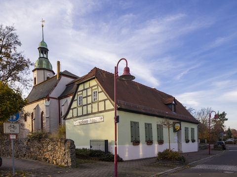 Dasd Bild zeigt das Turmuhrenmuseum im grünen Fachwerkhaus vor der Kirche.
