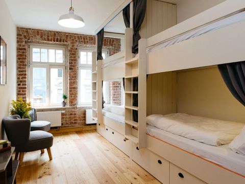 Blick auf ein helles und modernes Hostelzimmer mit zwei Etagenbetten und zwei Sesseln.
