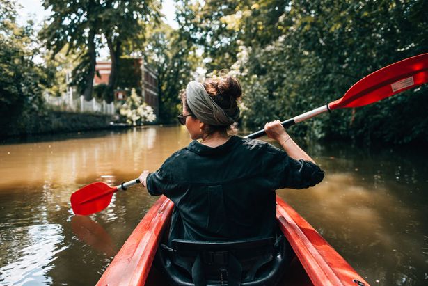 A young lady sitting in a canoe holding a paddle on a canal in Leipzig, water city Leipzig, boat hire Leipzig, canoe trip