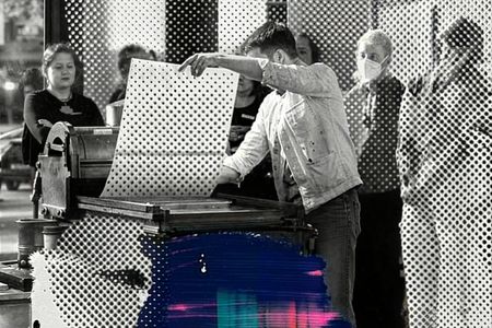 Ein Mensch demonstriert mit einem großen Blatt die Funktion einer historischen Druckerpresse