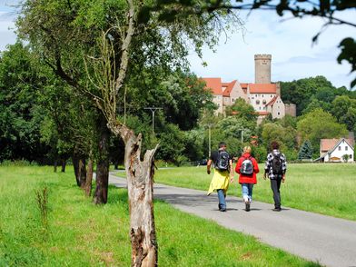Wandern in Gnandstein, zu sehen sind drei Wanderer mit Rucksäcken auf einem Fußweg, im Hintergrund sieht man die Burg Gnandstein © Andreas Schmidt